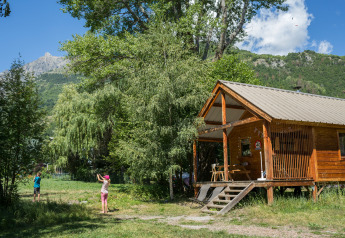 Dos niños juegan fuera de una cabaña de madera rodeada de naturaleza en Chalet Montana en Huttopia Vallouise, Francia.
