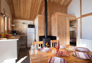 Interior del Chalet Montana en Huttopia Vallouise, Francia, con cocina, mesa de comedor y estufa de leña.