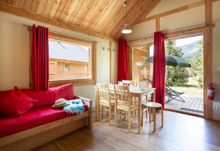 Hyggelig stue i Chalet Montana på Huttopia Vallouise, Frankrig, med træmøbler og rød indretning.