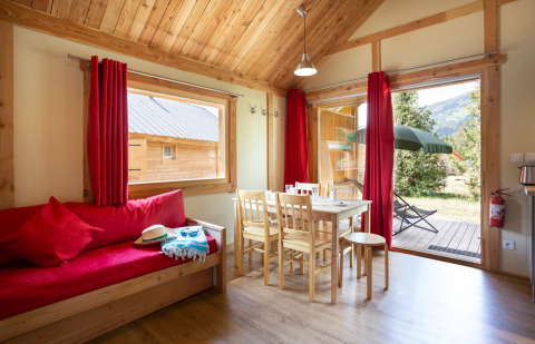 Acogedora sala de estar en Chalet Montana de Huttopia Vallouise, Francia, con muebles de madera y decoración roja.