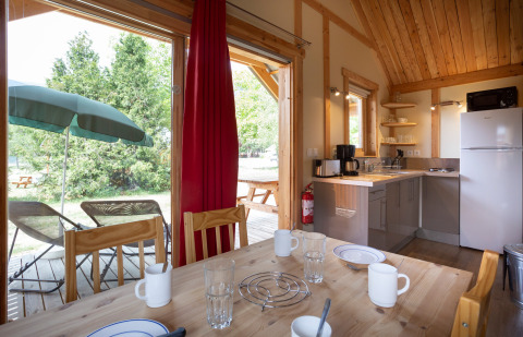 Vista interior del Chalet Montana en Huttopia Vallouise, con cocina, mesa de comedor y terraza exterior.