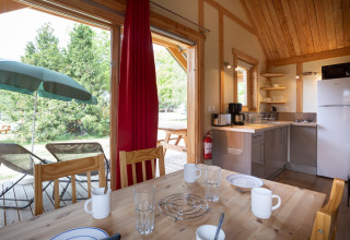 Vista interior del Chalet Montana en Huttopia Vallouise, con cocina, mesa de comedor y terraza exterior.