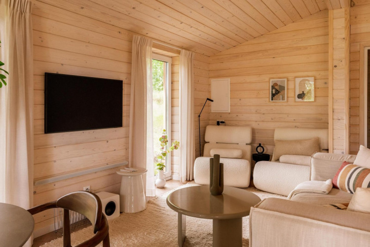 Sala de estar escandinava luminosa en Forresthouse Scandi, Wilsumer Berge, Alemania, con paneles de madera y decoración moderna.