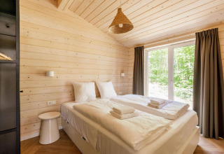 Dormitorio luminoso en Forresthouse Scandi, Wilsumer Berge, Alemania, con cama doble y grandes ventanas.