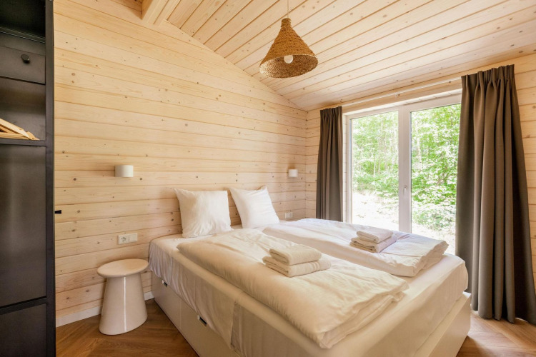 Dormitorio luminoso en Forresthouse Scandi, Wilsumer Berge, Alemania, con cama doble y grandes ventanas.