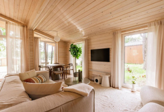 Interior de cabaña escandinava luminosa en Forresthouse Scandi, Wilsumer Berge, Alemania, con ventanas grandes y madera.