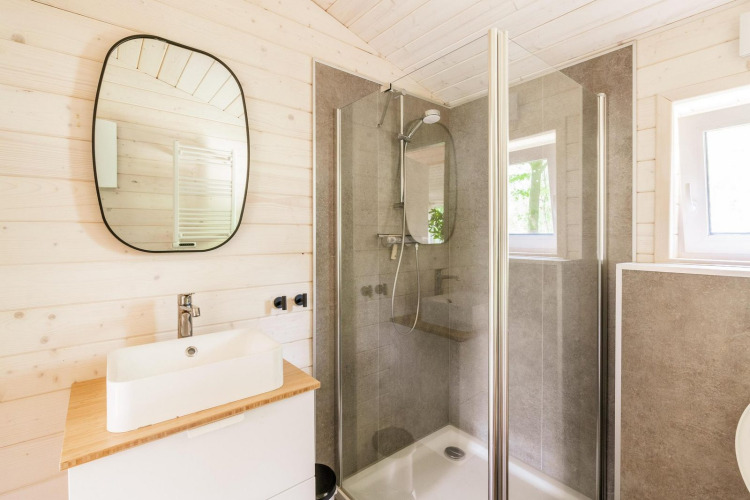 Baño luminoso en Forresthouse Scandi en Wilsumer Berge, Alemania, con ducha, lavabo y espejo modernos.