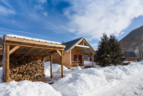 Cabañas de madera cubiertas de nieve y cobertizo de leña en Les chalets Huttopia de Bourg-St-Maurice en Francia.