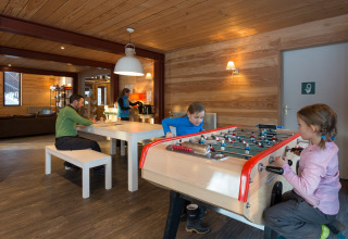 Kinderen spelen tafelvoetbal en volwassenen ontspannen in de lounge van Les chalets Huttopia de Bourg-St-Maurice.