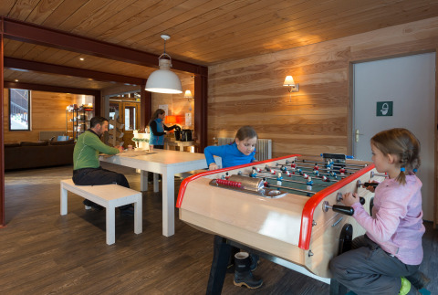 Niños juegan al futbolín mientras adultos descansan en la sala común de Les chalets Huttopia de Bourg-St-Maurice, Francia.
