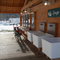 Zona de lavado exterior con varios lavabos grandes, dos bicicletas y un camping nevado al fondo.