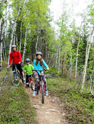 En familie cykler på en skovsti omgivet af grønne træer under deres ophold på en glampingferiepark.