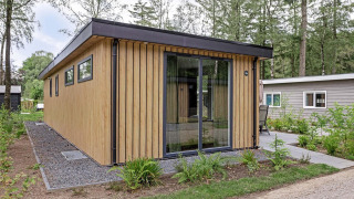 Moderna cabaña llamada Module Wood en Bospark Ede, Países Bajos, rodeada de árboles y vegetación.
