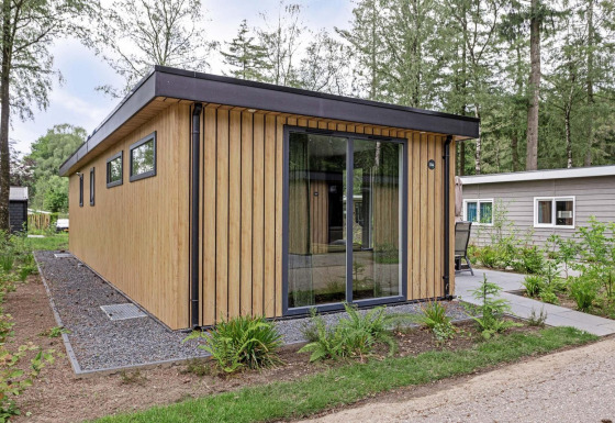 Moderna cabaña llamada Module Wood en Bospark Ede, Países Bajos, rodeada de árboles y vegetación.