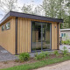 Moderne lodge ved navn Module Wood i Bospark Ede, Holland, omgivet af grønne træer og natur.