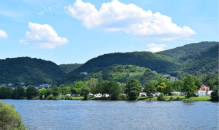Paisaje junto al río con zona de camping, colinas verdes y cielo azul cerca de Oberbronn, Grand Est, Francia.