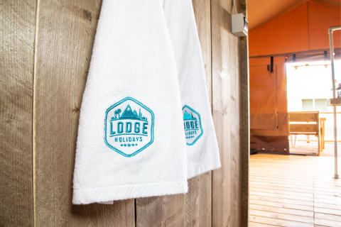 Asciugamani bianchi con logo 'Lodge Holidays' in una tenda safari presso Desert Lodge, Boutique Camping Heart of Nature, Croazia.