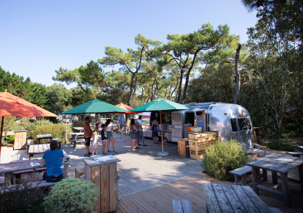 Buitencafé met foodtruck, tafels en parasols bij Huttopia Noirmoutier, Pays de la Loire, Frankrijk.