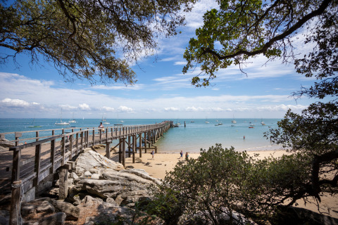 Ponton en bois sur la plage avec des voiliers au loin à Huttopia Noirmoutier, Pays de la Loire, France.