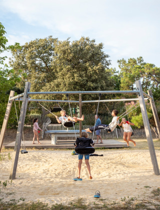 Niños jugando en columpios en el parque infantil de Huttopia Noirmoutier, Pays de la Loire, Francia.