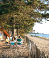Familia disfrutando en una mesa junto a su tienda en la playa de Huttopia Noirmoutier, Pays de la Loire, Francia.