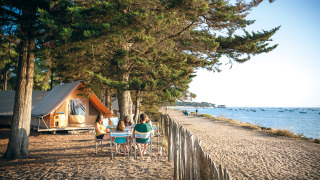 Familie sitzt an einem Tisch auf einem Campingplatz am Strand bei Huttopia Noirmoutier, Pays de la Loire.