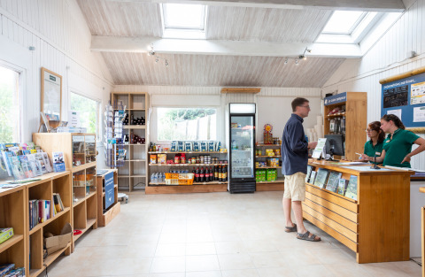 Recepción y tienda en Huttopia Noirmoutier con huéspedes y personal en Pays de la Loire, Francia.