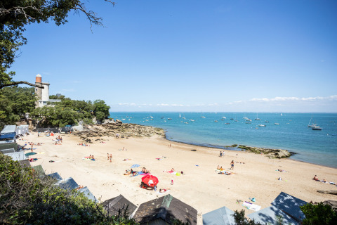 Escena de playa en Huttopia Noirmoutier, Pays de la Loire, Francia, con personas y barcos en el agua.