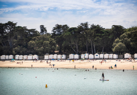 Playa con cabañas blancas y personas nadando y tomando el sol en Huttopia Noirmoutier, Pays de la Loire, Francia.