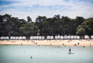 Strand tafereel met witte hutjes en mensen die zwemmen aan Huttopia Noirmoutier, Pays de la Loire, Frankrijk.