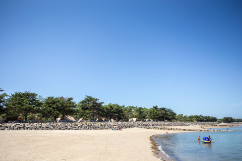 Playa de arena con tiendas y familias en Huttopia Noirmoutier, parque vacacional en Pays de la Loire, Francia.