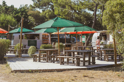 Buiten zitgedeelte met groene parasols en houten banken bij foodtrucks in Huttopia Noirmoutier, Frankrijk.