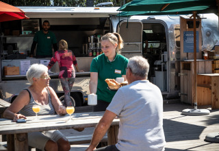 Medewerker serveert ontbijt aan twee gasten buiten aan een foodtruck bij Huttopia Noirmoutier, Frankrijk.