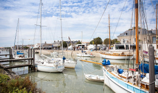 Segelboote im Hafen von Noirmoutier en l'île, Frankreich, mit Häusern und blauem Himmel im Hintergrund.