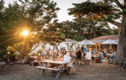 Udendørs middagsscene med familier og venner på picnicborde i Huttopia Ars-en-Ré, Nouvelle-Aquitaine.