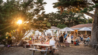 Escena al aire libre con familias cenando al atardecer en Huttopia Ars-en-Ré, Nouvelle-Aquitaine, Francia.