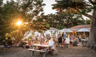 Escena al aire libre con familias cenando al atardecer en Huttopia Ars-en-Ré, Nouvelle-Aquitaine, Francia.