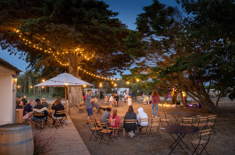 Evening outdoor gathering with string lights, people seated, at Huttopia Ars-en-Ré holiday park in France.