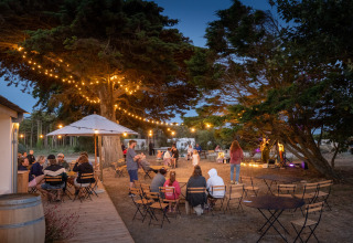 Soirée en plein air avec guirlandes lumineuses et convives au Huttopia Ars-en-Ré, Nouvelle-Aquitaine, France.