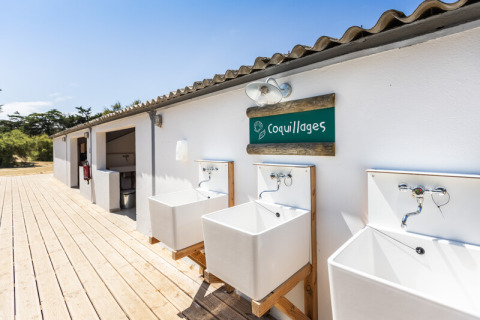 Buitenkraan en sanitairgebouw op Huttopia Ars-en-Ré vakantiepark, Frankrijk, onder blauwe lucht.