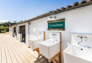 Udendørs vaskepladser og sanitetsbygning under blå himmel på Huttopia Ars-en-Ré i Frankrig, sommerstemning.