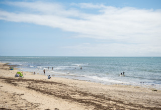 Strandscene nær Ars-en-Ré i Nouvelle-Aquitaine, Frankrig, med få mennesker, hav og let skyet himmel.
