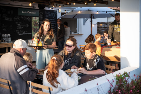 Una familia disfruta de una comida al aire libre mientras una camarera sirve bebidas en Huttopia Ars-en-Ré, Francia.