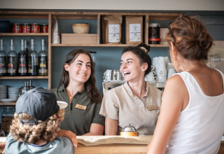 To smilende medarbejdere taler med gæster ved receptionen på Huttopia Ars-en-Ré feriepark i Frankrig.