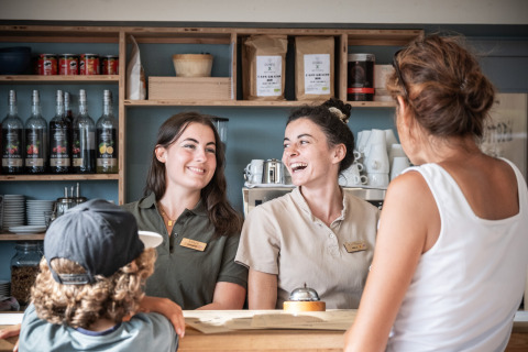 Two smiling staff members greet guests at the reception desk of Huttopia Ars-en-Ré holiday park in France.