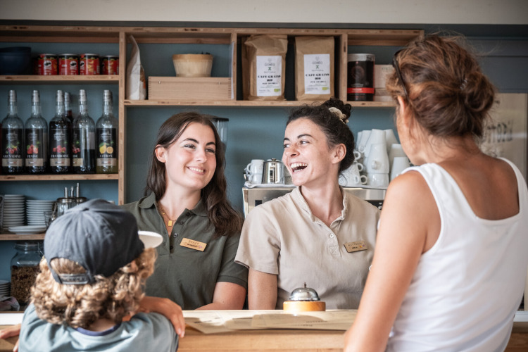 Two smiling staff members greet guests at the reception desk of Huttopia Ars-en-Ré holiday park in France.