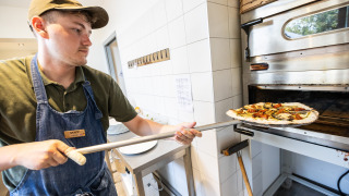 Un empleado de Huttopia Ars-en-Ré mete una pizza en el horno en el parque vacacional de Nouvelle-Aquitaine.