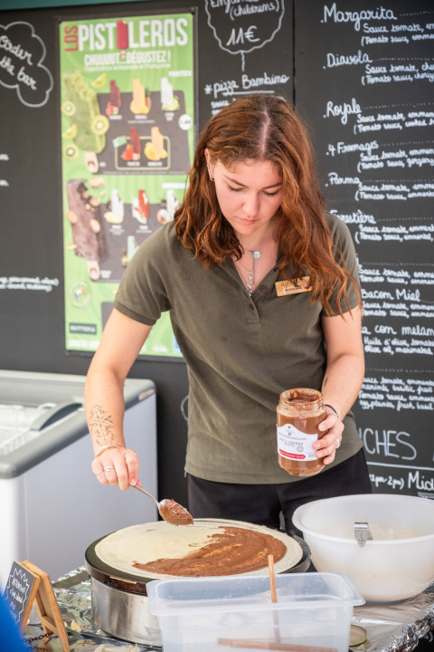 Una donna spalma crema al cioccolato su una crêpe in uno stand gastronomico a Huttopia Ars-en-Ré, Francia.