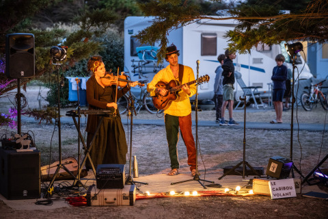 Músicos actúan al aire libre en el parque vacacional Huttopia Ars-en-Ré en Nouvelle-Aquitaine, Francia, de noche.