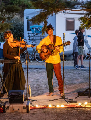 Músicos actúan al aire libre en el parque vacacional Huttopia Ars-en-Ré en Nouvelle-Aquitaine, Francia, de noche.